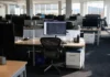 AI Security in 2027: 54% of Firms Can’t Limit AI Agent Access Brightly lit open-plan office with rows of desks and monitors; one active monitor at a central workstation.