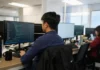 Vulnerability Remediation Gap: 79% Breached by Known Weaknesses A security analyst sits at a desk, focused on a monitor displaying a vulnerability tracking dashboard in a bright office.
