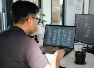 AI Governance Gap: 81% of CISOs Fear Agents They Can’t Fully See A person with glasses sits at a desk, focused on a laptop displaying data, in a bright modern office.