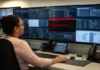 Medusa Ransomware Hits 500 Critical Infrastructure Orgs by Buying Access A woman sits at a desk, focused on multiple screens displaying network data and remote-access session tiles.