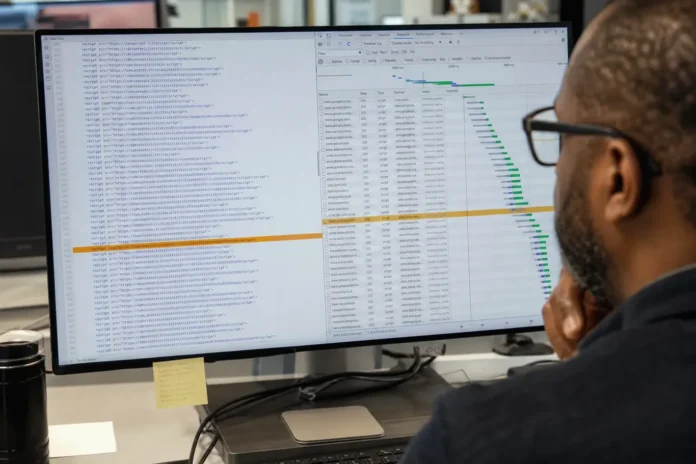csi-3bf2517811cf9b01-featured A person with glasses views a brightly lit code editor displaying a JavaScript dependency list, with one entry highlighted in amber.