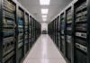 Brightly lit data center aisle with rows of rack-mounted network switches and security appliances in black cabinets.
