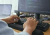 Anthropic’s AI Security Tests Broke Into Three Real Companies Close-up of hands mid-keystroke on a keyboard, with a blurred monitor displaying code in the background.