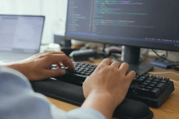 Close-up of hands mid-keystroke on a keyboard, with a blurred monitor