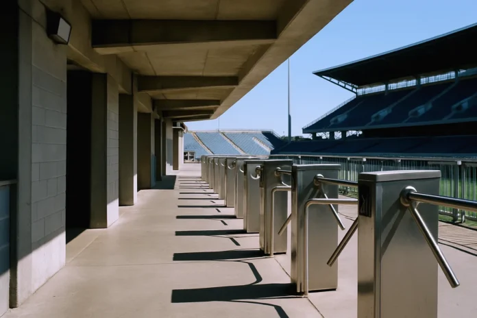 csi-7ff4e664f8602ae7-featured Empty stadium concourse in bright daylight, featuring turnstile barriers and a view of the stands, shot from ground level.