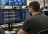 A person sits at a workstation in a bright security operations center, facing dual monitors displaying data and alerts.