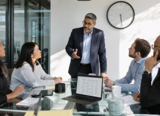 The Biggest CISO Challenges of 2026: 73% Still Aren’t Ready for a Major Attack A CISO in business attire stands at a glass conference table, discussing with colleagues around a laptop and clock on the wall.