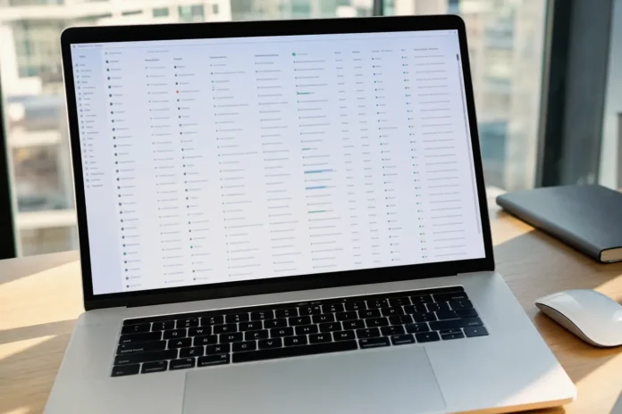 A close-up of a MacBook Pro on a clean desk, displaying a spreadsheet in a bright modern office setting.