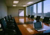 CISO Board Reporting: Gartner Says Drop the Dashboard, Use Financial Statements Brightly lit corporate boardroom with a polished conference table, empty chairs, and a presentation board at the front.