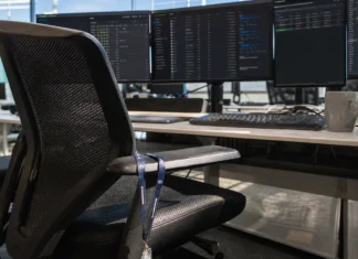 Finance Lets AI Security Automation Act Alone; Attackers Use AI Right Back A close-up of an empty operator's chair at a security operations desk with multiple monitors and a staff lanyard.