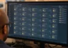 BlueMoon Zero-Day Exploit Kit Chains Chrome and Windows Flaws A person with glasses views a widescreen monitor displaying a software update-management console with rows of status tiles.