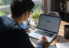 Lenovo Flaw Exposed 5,000 Dropbox Accounts Through Identity Federation A person leans toward a laptop on a wooden desk, with a plant and books nearby, in natural light.