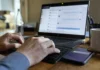 Your MFA Won’t See This: Identity Security’s Blind Spot Inside Teams and Slack Close-up of hands typing on a keyboard, with a laptop screen displaying a chat panel and a smartphone nearby.