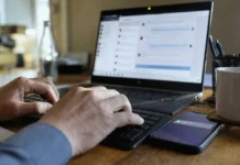 Your MFA Won’t See This: Identity Security’s Blind Spot Inside Teams and Slack Close-up of hands typing on a keyboard, with a laptop screen displaying a chat panel and a smartphone nearby.