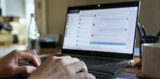 Close-up of hands typing on a keyboard, with a laptop screen displaying a chat panel and a smartphone nearby.